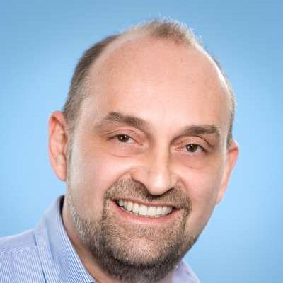 Ein glatzköpfiger Mann mit Bart lächelt in die Kamera.