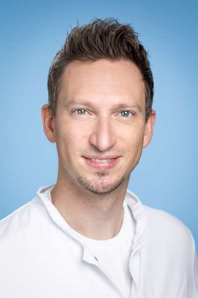 Ein Mann im weißen Laborkittel lächelt in die Kamera.