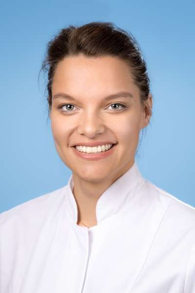 Eine Frau in einem weißen Laborkittel lächelt in die Kamera.