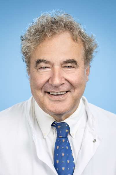 Ein Mann in einem weißen Kittel und einer blauen Krawatte lächelt in die Kamera.