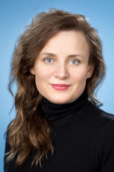 Eine Frau in einem schwarzen Rollkragenpullover lächelt in die Kamera.