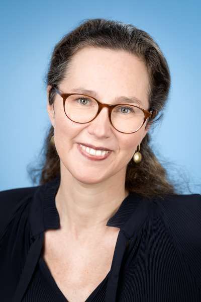 Eine Frau mit Brille und Ohrringen lächelt in die Kamera.