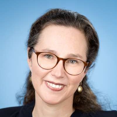 Eine Frau mit Brille und Ohrringen lächelt in die Kamera.