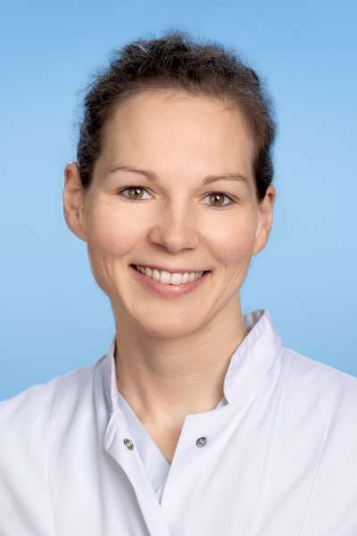 Eine Frau in einem weißen Laborkittel lächelt in die Kamera.