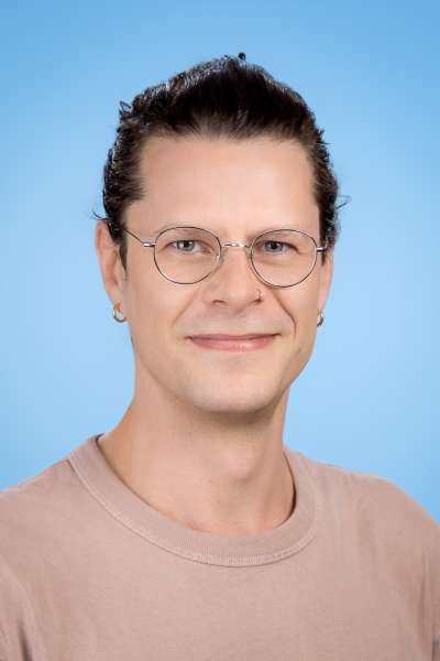 Ein Mann mit Brille und rosa Hemd lächelt in die Kamera.