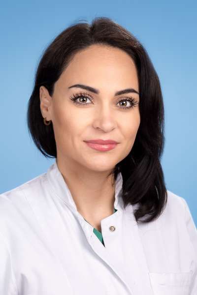 Eine Frau in einem weißen Laborkittel steht vor einem blauen Hintergrund.