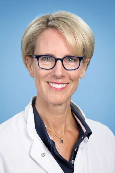 Eine Frau mit Brille und weißem Kittel lächelt in die Kamera.