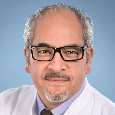 Ein Mann mit Brille und Bart trägt einen weißen Mantel und eine Krawatte.