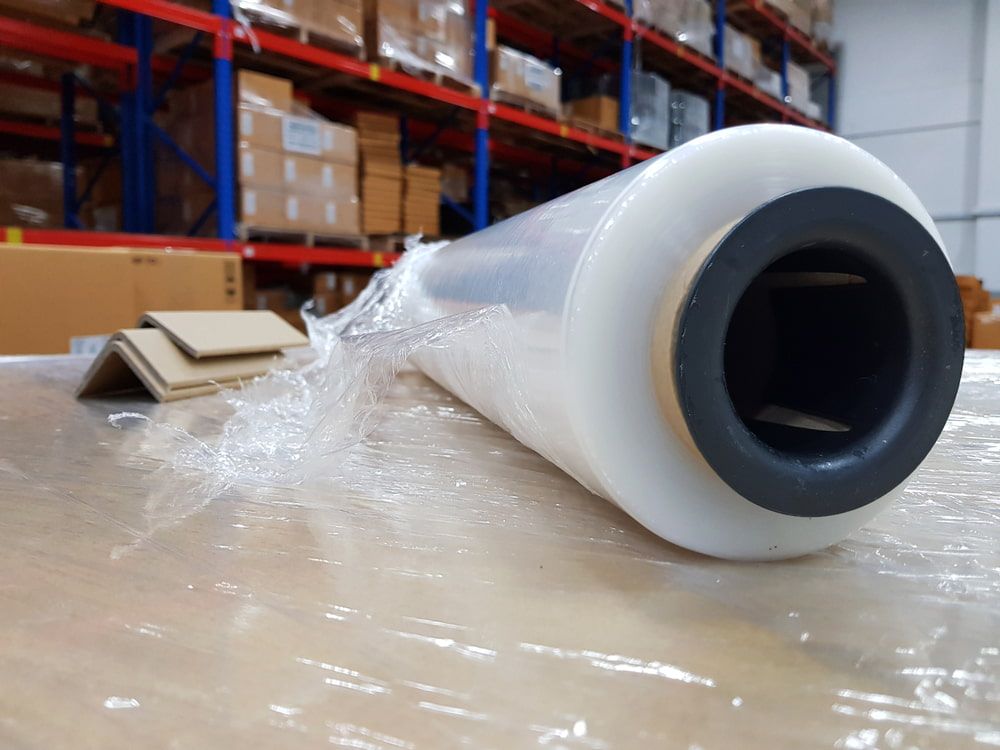 Roll of clear plastic stretch wrap with black and white ends on a table in a warehouse.