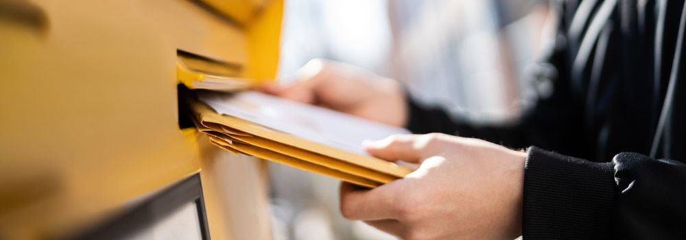 Person putting envelopes into a yellow mailbox.