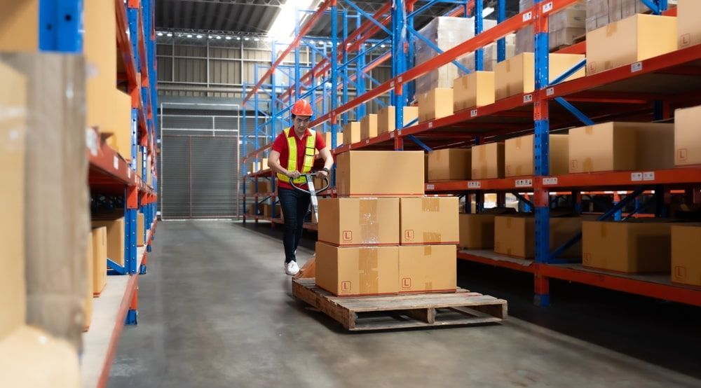 Warehouse worker moving boxes on a pallet with a manual pallet jack.