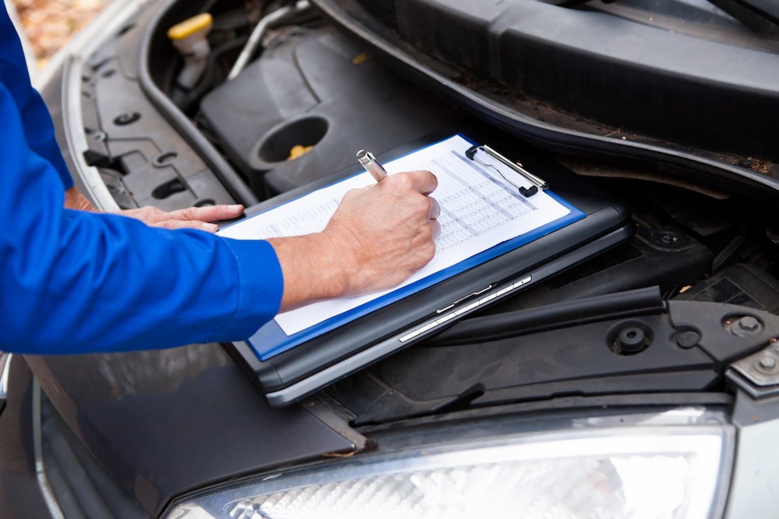A Mechanic Is Writing on A Clipboard Under the Hood of A Car — AJ Automotive Services Bowral in Bowral, NSW