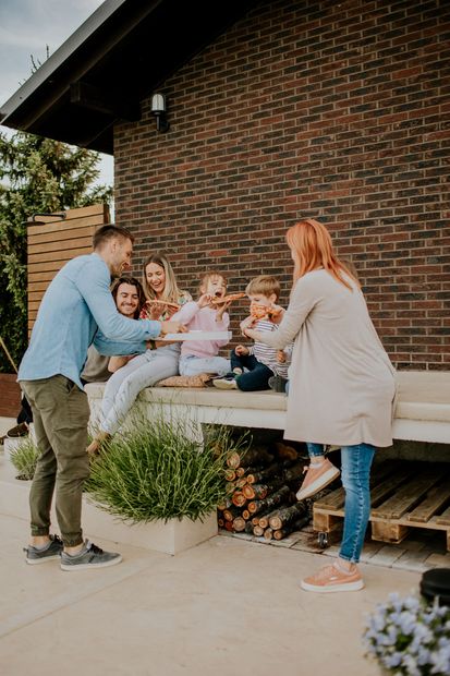 Family sitting on a bench near a brick building, smiling and eating.