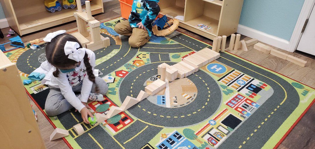 A little girl is playing with wooden blocks on a rug.