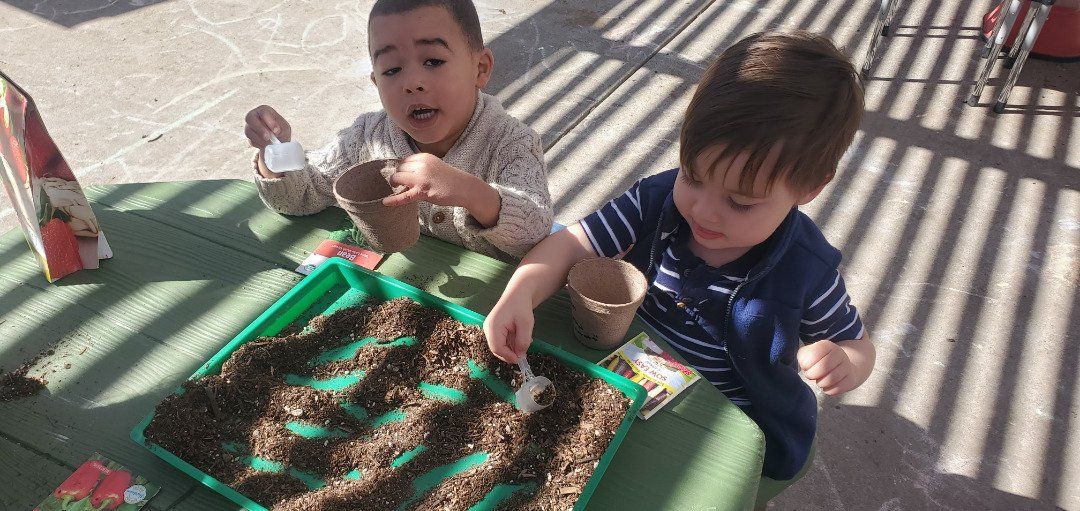 Two young boys are sitting at a table playing with dirt