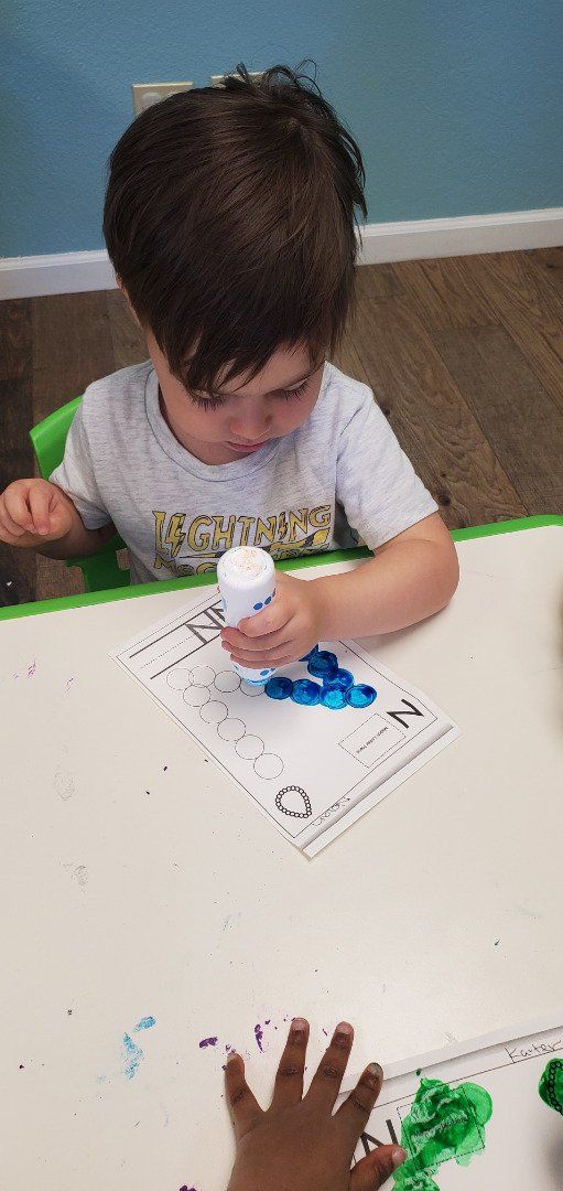 A young boy is sitting at a table holding a glue stick.
