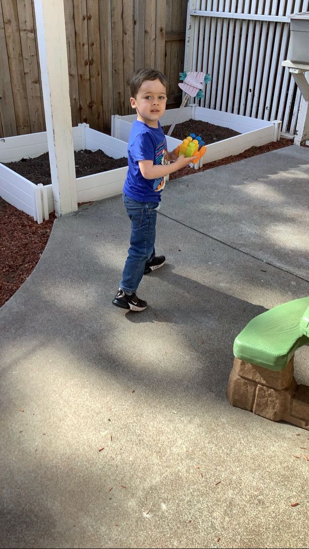 A young boy is standing on a sidewalk holding a toy.