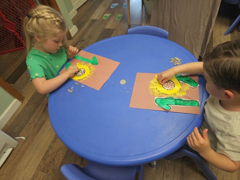 A boy and a girl are sitting at a table making sunflowers