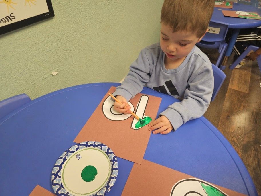A young boy is painting the letter c on a piece of paper