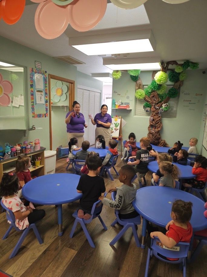 A group of children are sitting at blue tables in a classroom