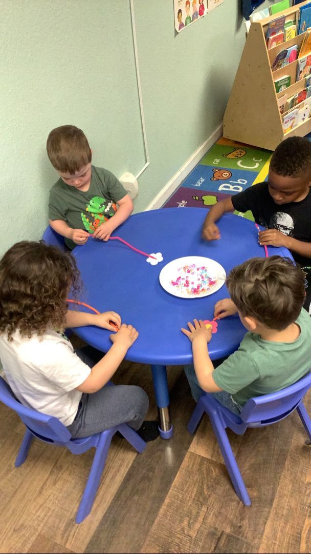 A group of young children are sitting around a blue table.