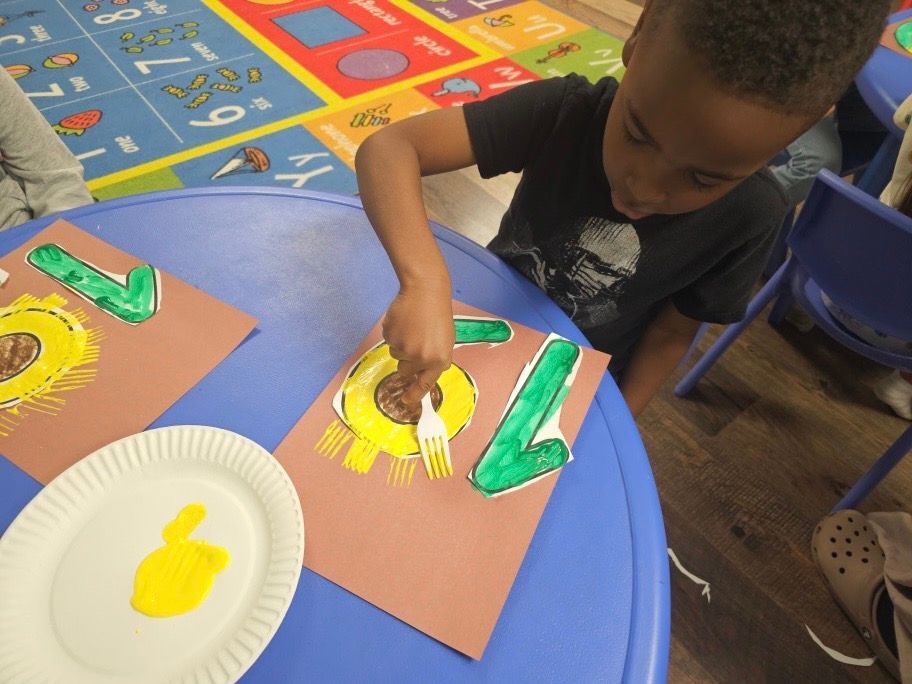 A young boy is sitting at a table painting letters with yellow and green paint