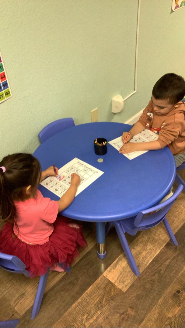 A boy and a girl are sitting at a blue table drawing
