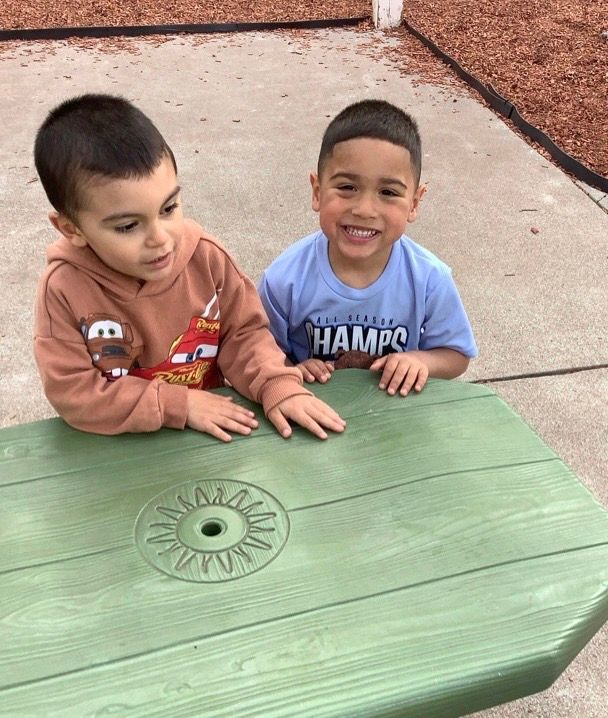 Two young boys are sitting at a green picnic table