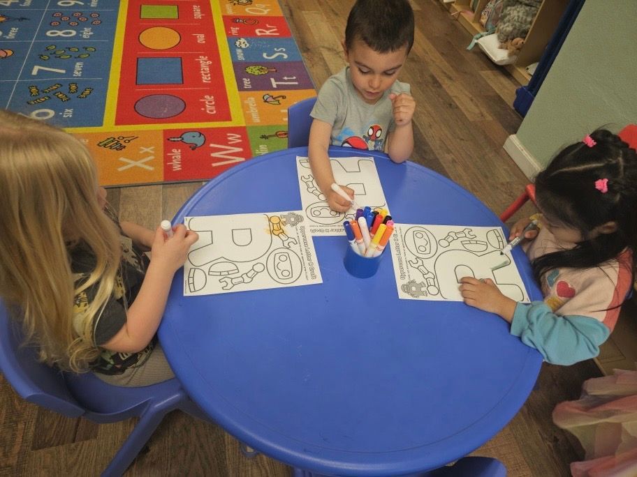 Three children are sitting at a blue table coloring