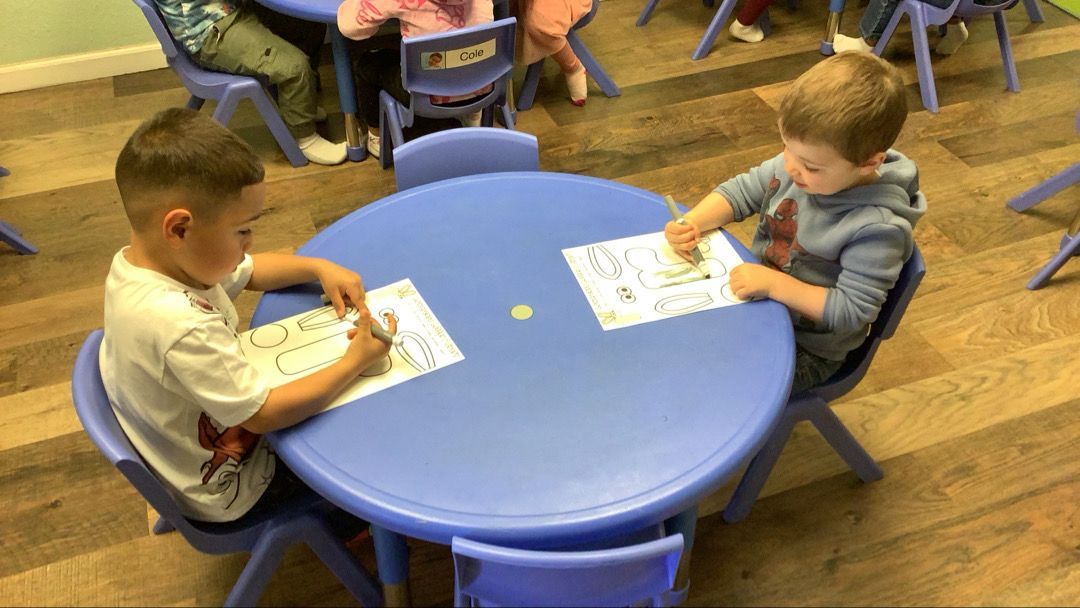 Two young boys are sitting at a blue table in a classroom