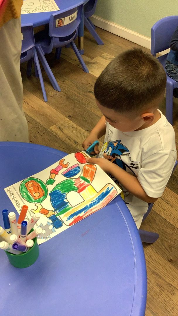 A young boy is sitting at a table cutting a piece of paper with scissors