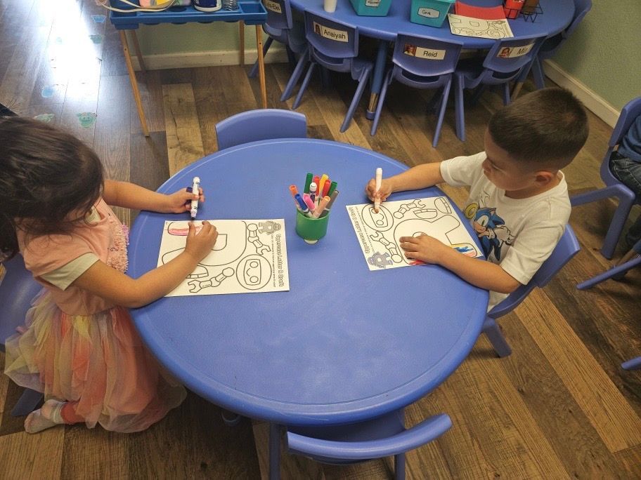 A boy and a girl are sitting at a table drawing with markers
