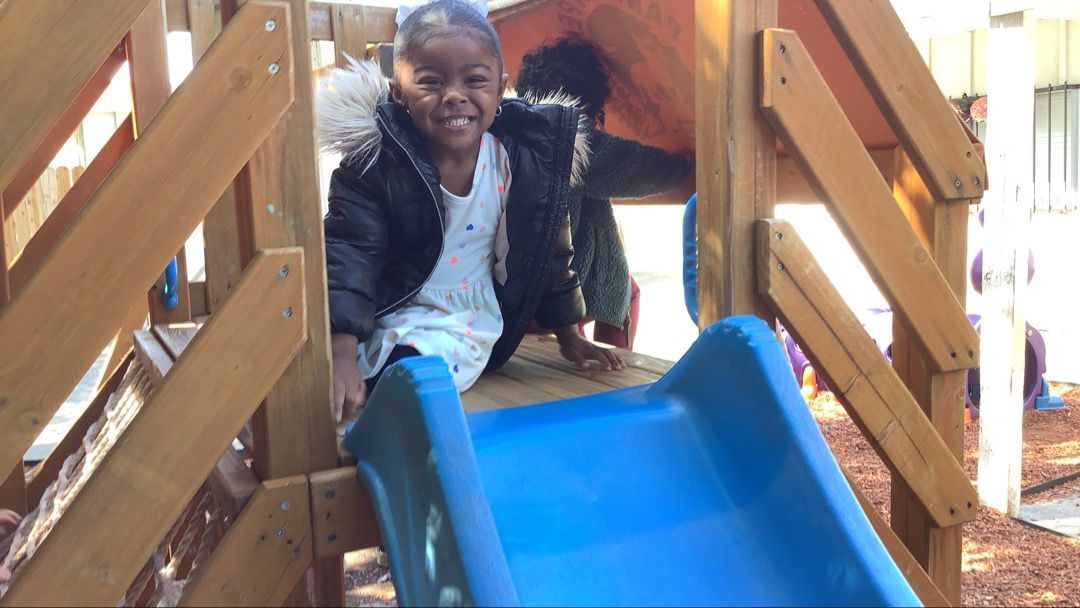 A little girl is sitting on a slide at a playground