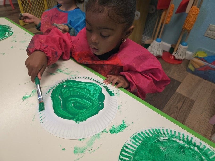 A little girl is painting a paper plate with green paint