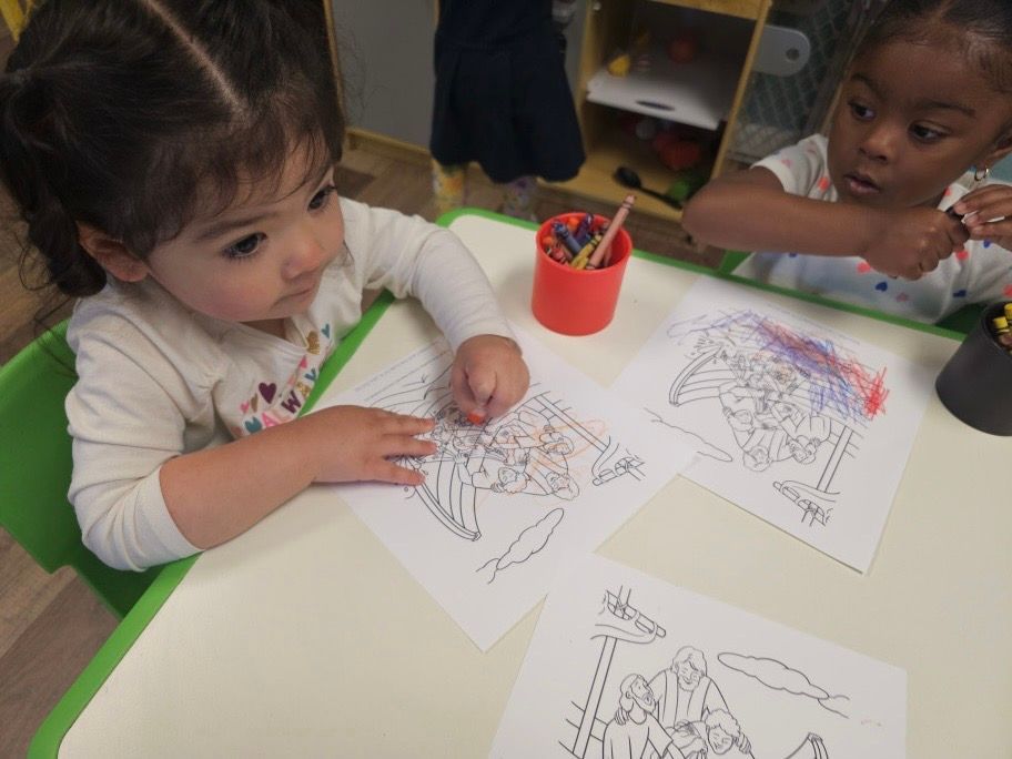 Two little girls are sitting at a table drawing with crayons