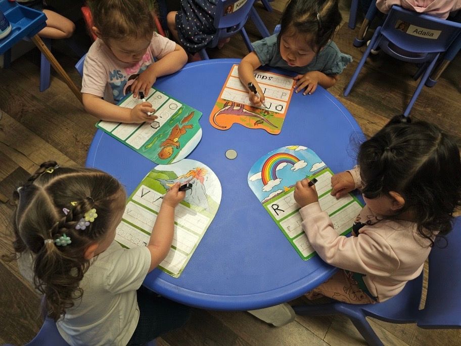 A group of young girls are sitting around a blue table writing on cards
