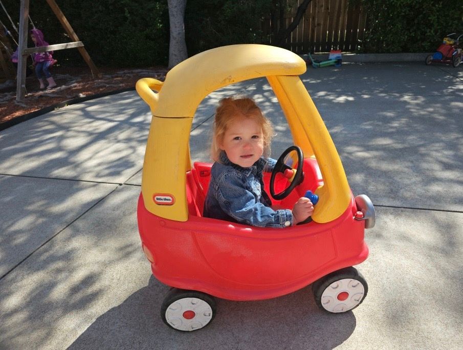 A little girl is sitting in a red and yellow toy car
