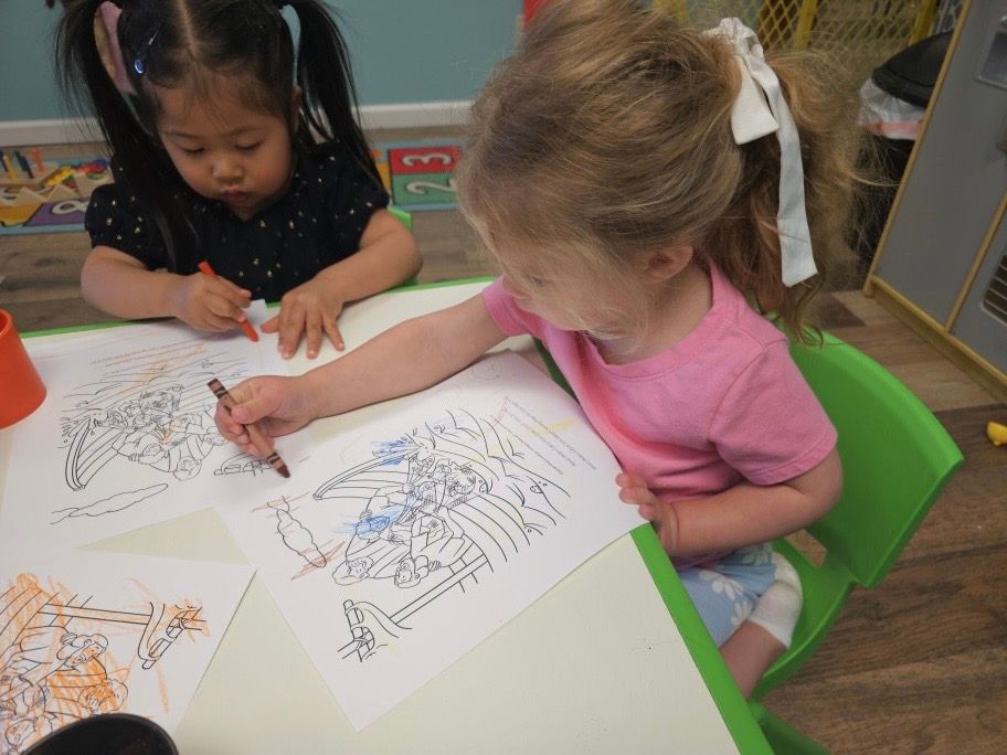 Two little girls are sitting at a table drawing with crayons
