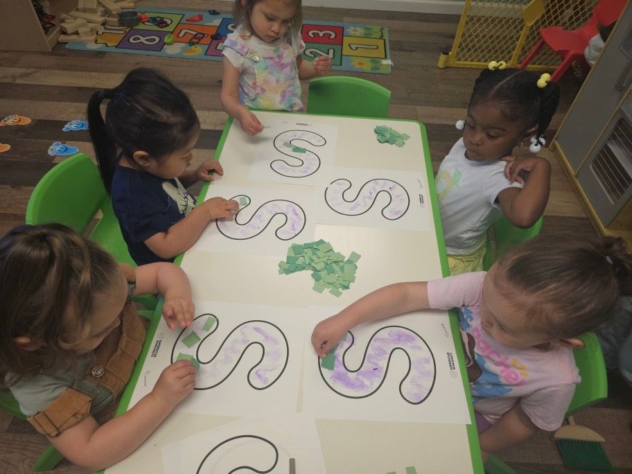 A group of young girls are sitting at a table drawing swirls on a piece of paper