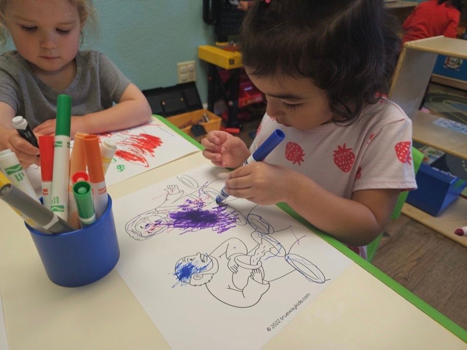 Two little girls are sitting at a table drawing with markers