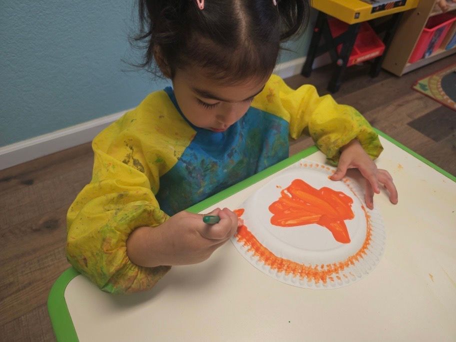 A little girl is painting on a paper plate with orange paint