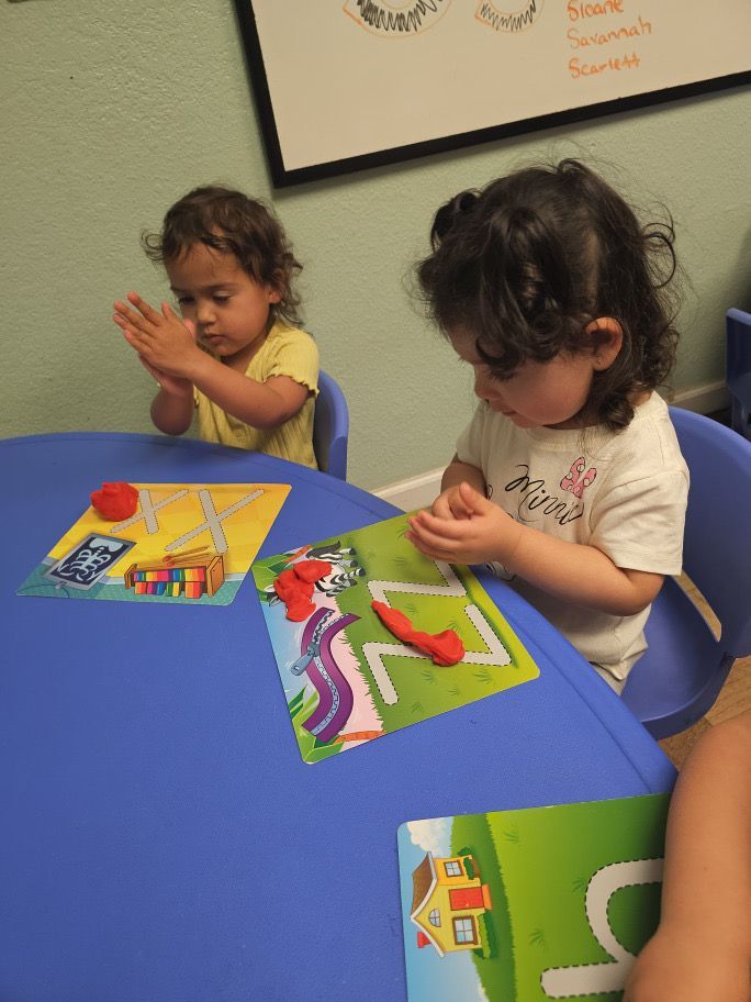 Two little girls sit at a table playing with clay
