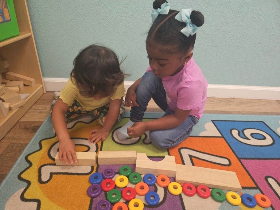 Two little girls are playing with wooden blocks on the floor