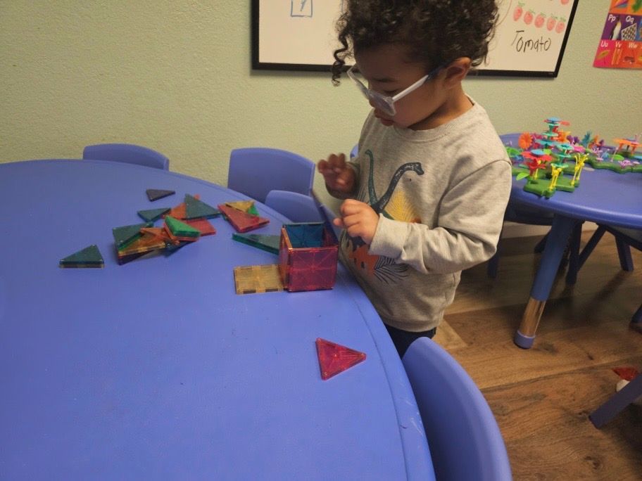A young boy wearing glasses is playing with blocks on a blue table
