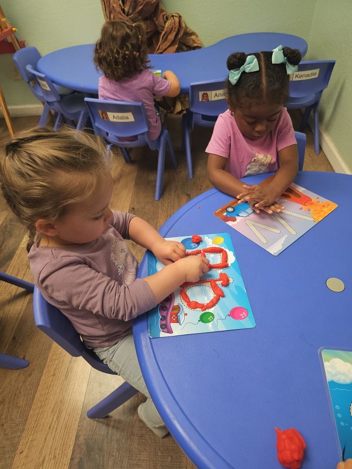 Two little girls are sitting at a table playing with clay