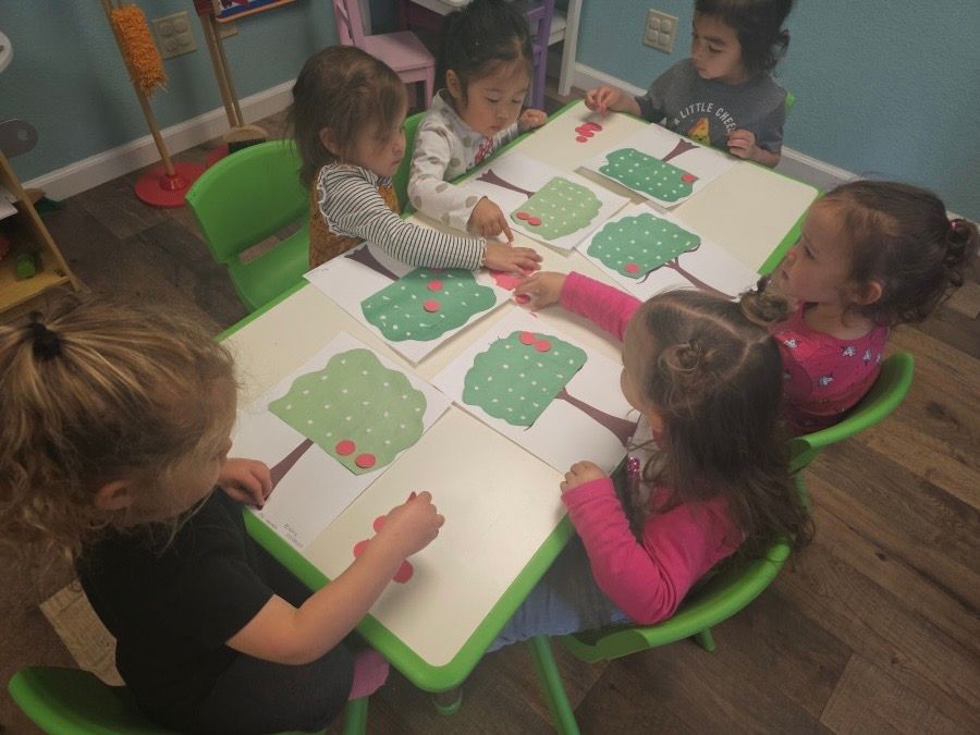 A group of children are sitting at a table playing with paper trees