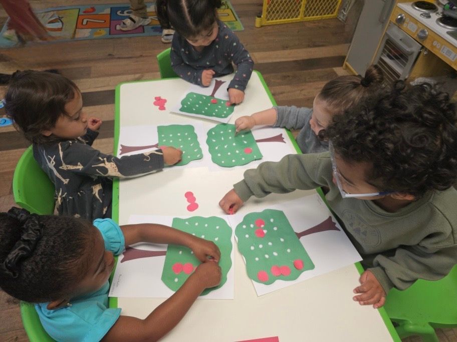 A group of children are sitting at a table playing with paper trees
