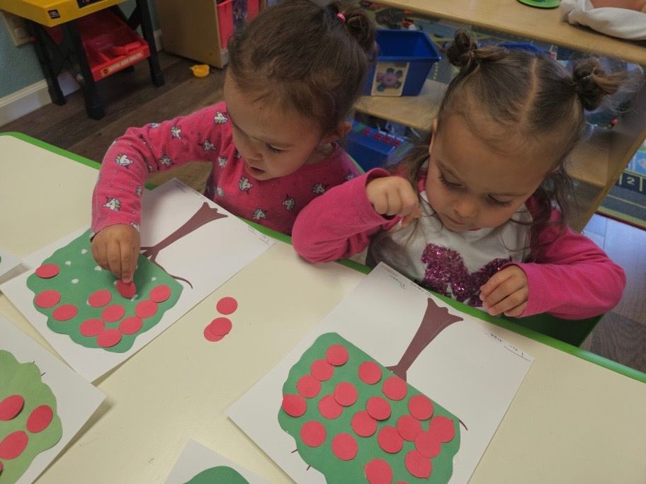 Two little girls are sitting at a table playing with paper crafts