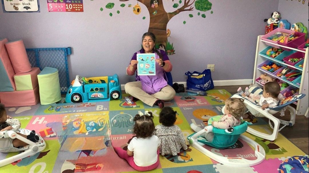 A woman is sitting on the floor reading a book to a group of babies.