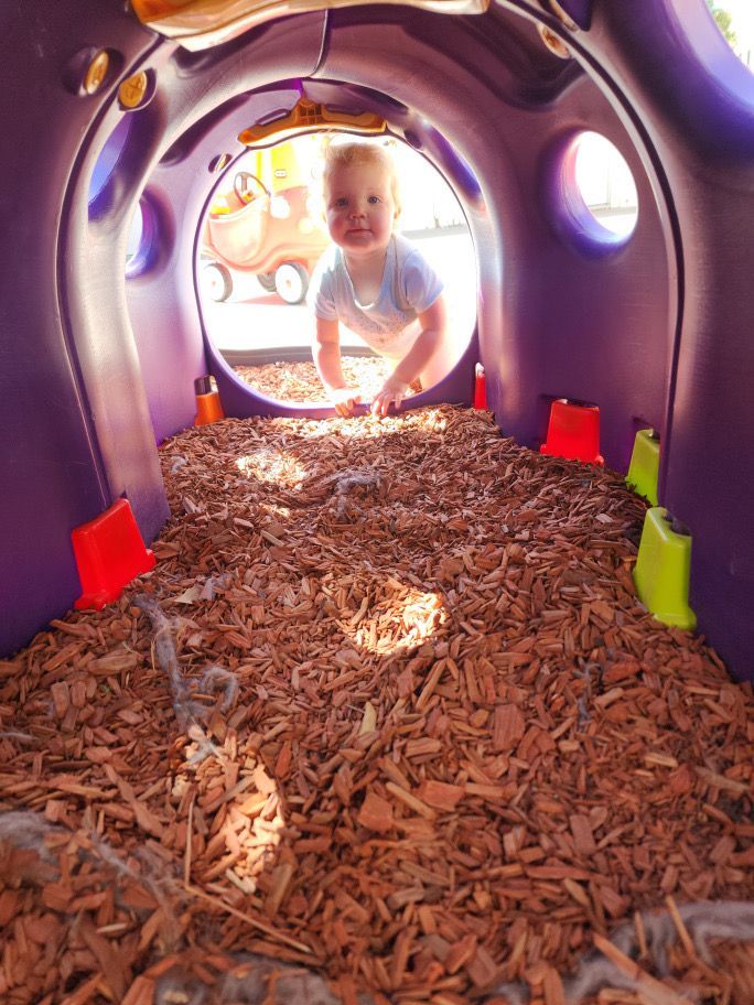 A baby is crawling through a tunnel of wood chips